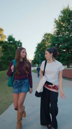 Two young women walking outdoors on a paved path with trees in the background