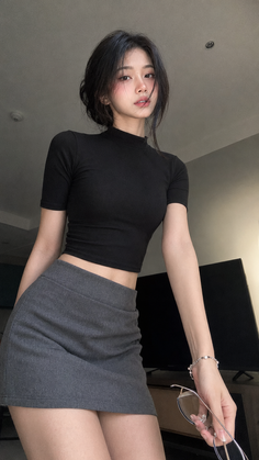 Woman in a black crop top and gray mini skirt holding glasses indoors