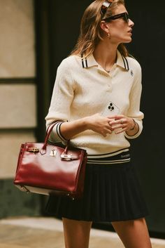 Woman in a polo shirt and pleated skirt holding a red handbag and phone
