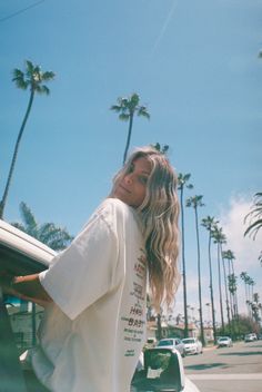 Woman with long blonde hair in an oversized t-shirt on a street with palm trees