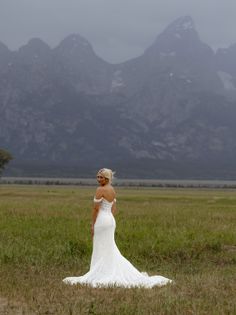 Woman in a white wedding dress in a grassy field with mountains in the background
