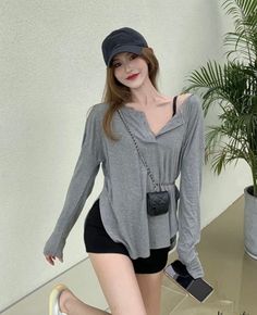 Woman in a gray long-sleeve shirt and black shorts with a baseball cap