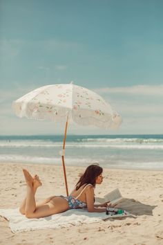 Woman in a floral swimsuit reading a book on a beach under an umbrella
