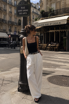 Woman in white pants and a black top standing on a street in front of a cafe