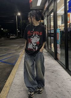 Person in baggy jeans and a graphic t-shirt standing on a street at night