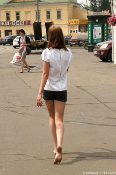Woman with short hair walking barefoot on a street in a white shirt and shorts