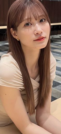 Woman with long brown hair and bangs wearing a neutral-colored dress