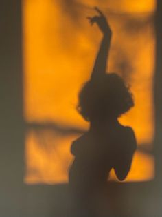 Shadow of a person with short hair and raised arm against a warm orange background