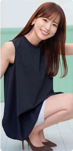 Woman in a black top and white shorts, squatting and smiling indoors