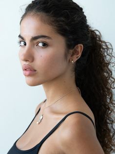 Woman with curly black hair wearing a black top and jewelry, looking over her shoulder