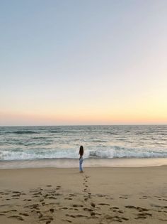 Woman with long hair standing on a beach at sunset, looking at the ocean