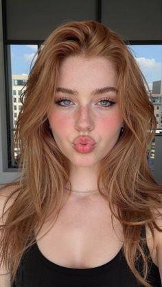 Woman with red hair and blue eyes making a kissy face indoors