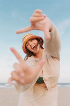 Woman in a bucket hat and bikini top making a frame with her hands on a beach