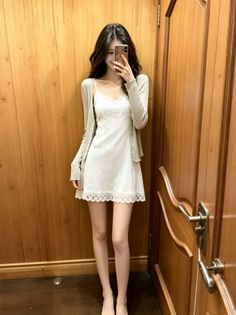 Woman in a white dress and cardigan taking a full body selfie indoors