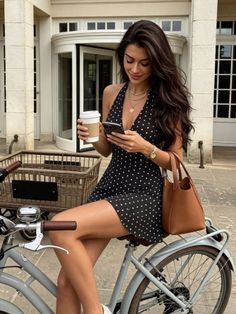 Woman in a polka dot dress sitting on a bicycle, holding coffee and phone