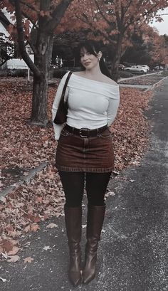 Woman in an off-shoulder top, mini skirt, and knee-high boots outdoors with autumn leaves