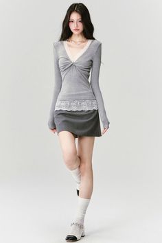 Woman with long dark hair wearing a gray top and mini skirt with lace trim