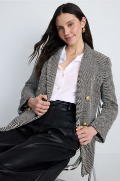 Woman with long dark hair wearing a blazer and black pants, sitting indoors