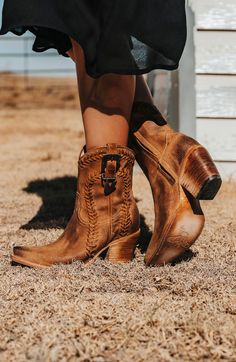 Person wearing brown cowboy boots and a short black dress on dry grass