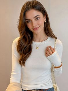 Woman with long brown hair wearing a white long-sleeve top and gold jewelry
