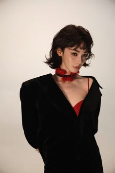 Woman with short hair wearing a black jacket and red top with a choker