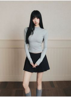 Woman with long black hair wearing a grey top and black pleated skirt indoors