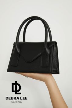 A black leather handbag held by a hand against a white background