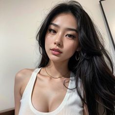 Woman with long dark hair and freckles wearing a white tank top and gold jewelry