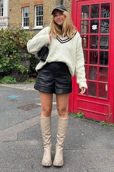 Woman in a cable knit sweater and leather shorts standing by a red telephone booth