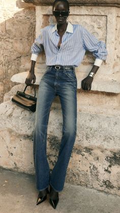 Person in a striped shirt and jeans leaning against a stone wall