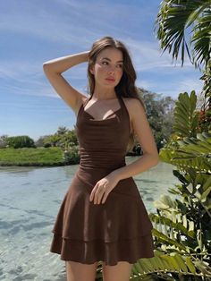Woman in a brown dress standing by clear water with tropical plants