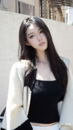 Woman with long black hair wearing a white cardigan and black top outdoors