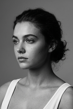 Woman with dark hair in an updo wearing a white tank top, looking to the side