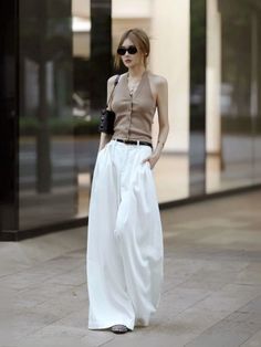 Woman in a halter top and wide leg pants with sunglasses and a shoulder bag