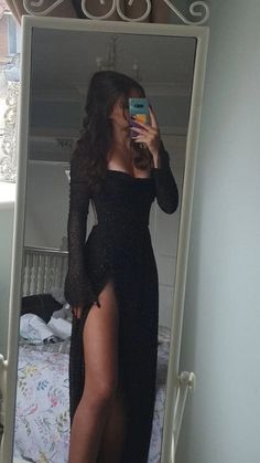 Woman in a black dress with a high slit taking a mirror selfie