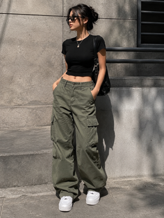 Woman in a black crop top and green cargo pants with sunglasses and a messy bun
