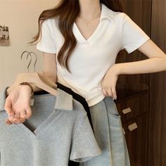 Woman in a white polo shirt and denim skirt holding a grey shirt on a hanger