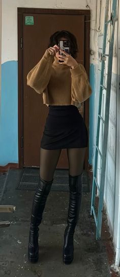 Person in a cropped sweater, mini skirt, and thigh-high boots taking a mirror selfie