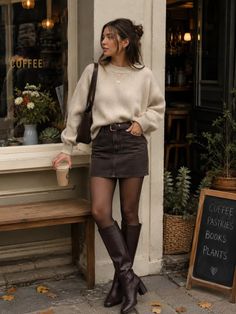 Woman in a sweater and mini skirt holding coffee outside a coffee shop