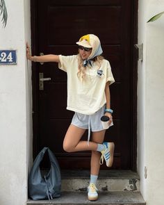 Woman in a baseball cap and head scarf leaning against a door with a coffee cup