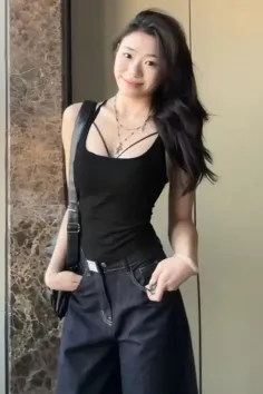 Woman with long dark hair wearing a black top and wide leg jeans indoors