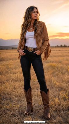 Woman in a fringe jacket and cowboy boots standing in a field at golden hour