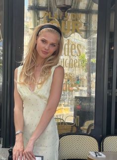 Blonde woman in a light floral dress and headband standing outside a cafe