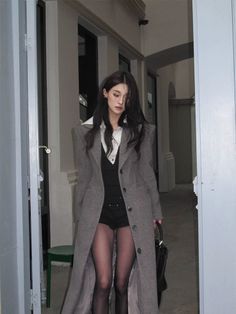 Woman in a long gray coat, black shorts, and tights indoors