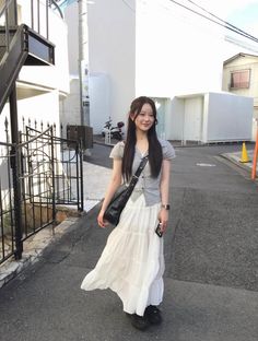 Woman with long hair wearing a white skirt and plaid shirt on a street