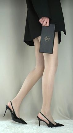 Person in a black dress and high heels holding a black box