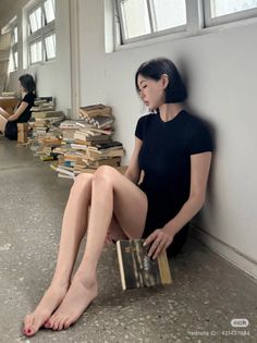 Woman with short hair in a black dress sitting on the floor with books