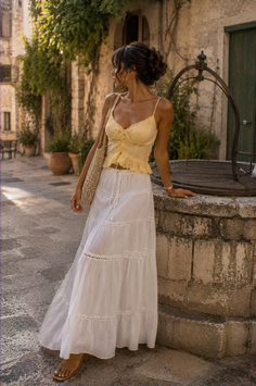 Woman in a long white skirt and yellow top standing by an old well