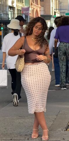 Woman with curly hair in a brown top and polka dot skirt on a street