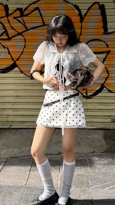 Woman in a white polka dot skirt and blouse standing in front of a graffiti wall